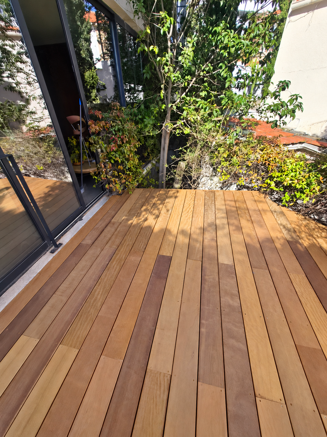 Terrasse en bois exotique au pied d'une baie vitrée et d'un jardin arboré